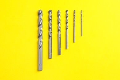 Different drill bits on yellow background, flat lay