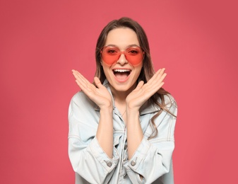Portrait of emotional young woman with heart shaped sunglasses on color background