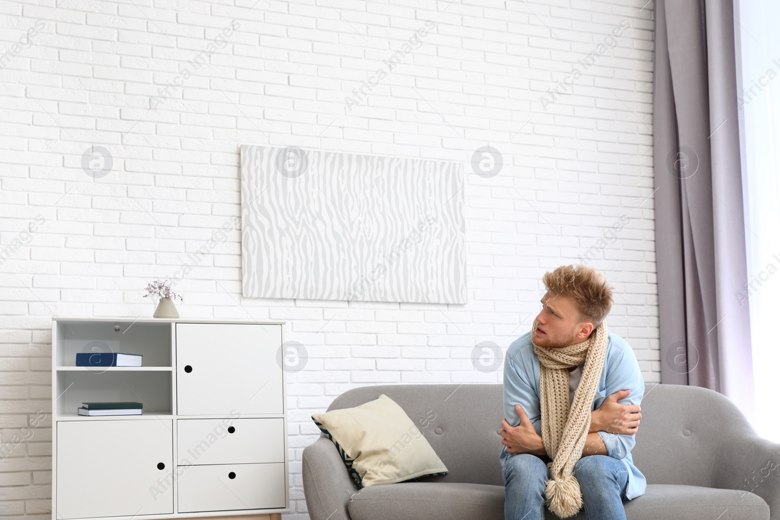 Photo of Young man in scarf suffering from cold at home. Air conditioner malfunction