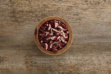 Photo of Bowl with dry kidney beans on old wooden table, top view