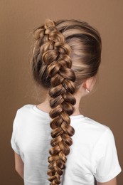 Little girl with braided hair on light brown background, back view