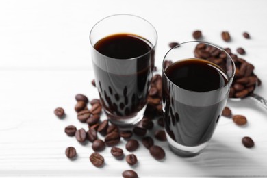 Photo of Shot glasses of coffee liqueur and beans on white table, closeup. Space for text