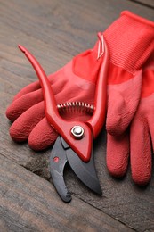 Photo of Pair of red gardening gloves and secateurs on wooden table