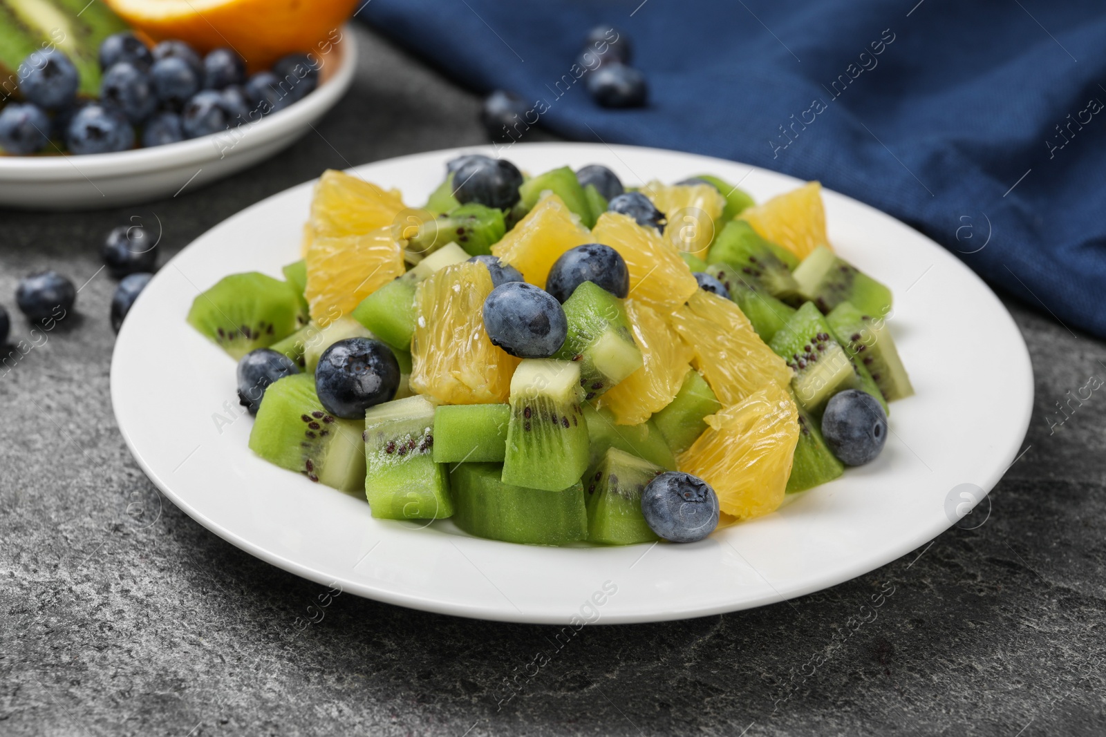 Photo of Plate of tasty fruit salad on grey textured table, closeup