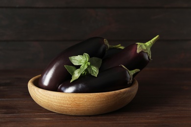 Photo of Ripe purple eggplants and basil on wooden table