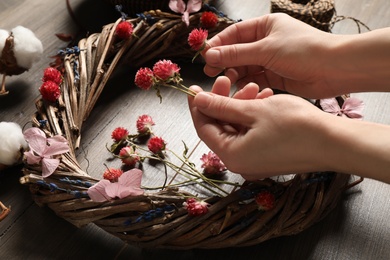 Photo of Florist making wreath with dried flowers at wooden table, closeup
