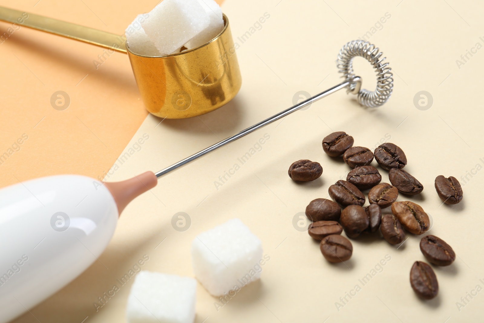 Photo of Milk frother wand, coffee beans and sugar cubes on color background, closeup