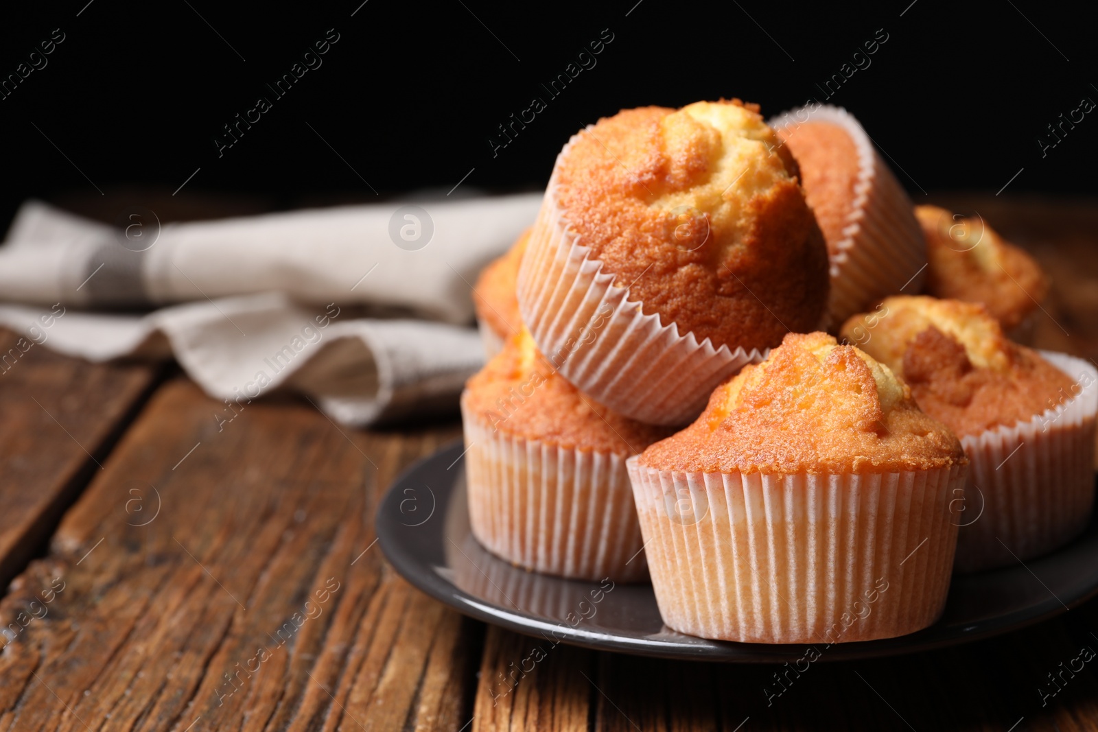 Photo of Delicious sweet muffins on wooden table against dark background, closeup. Space for text