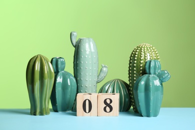 Photo of Stylish ceramic cactuses and wooden block calendar on table against color background. 8th of March - International Women's Day