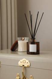 Photo of Aromatic reed air freshener and candle on suitcase indoors
