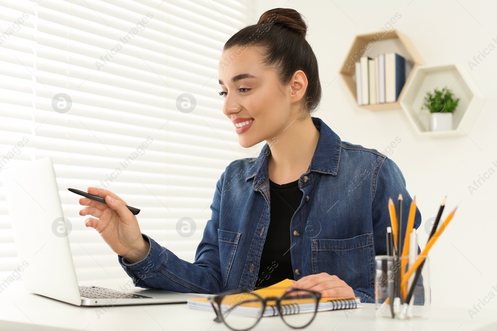 Photo of Home workplace. Happy woman working on laptop at white desk in room