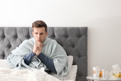 Sick young man with cough suffering from cold in bed