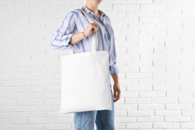 Woman with white textile bag near brick wall, closeup. Space for design