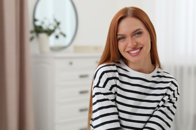 Photo of Portrait of beautiful young woman with red hair at home. Attractive lady smiling and looking into camera. Space for text