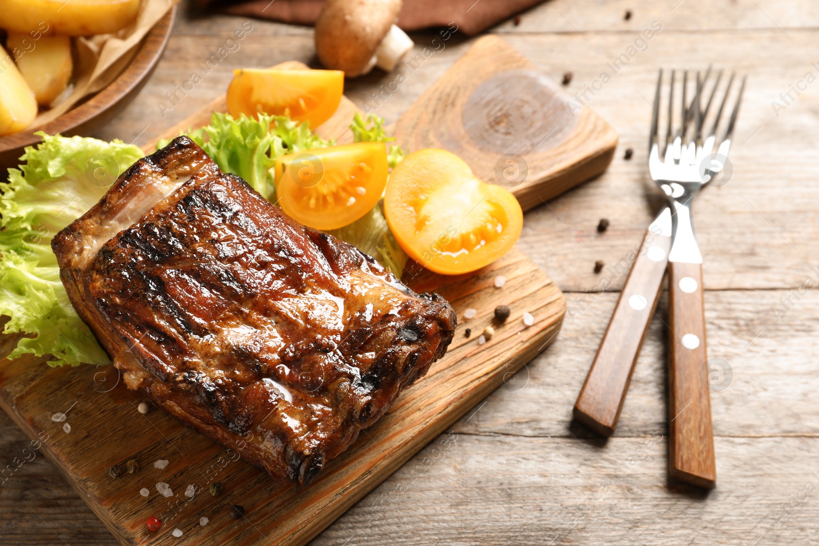 Photo of Delicious barbecued ribs served with garnish on wooden board