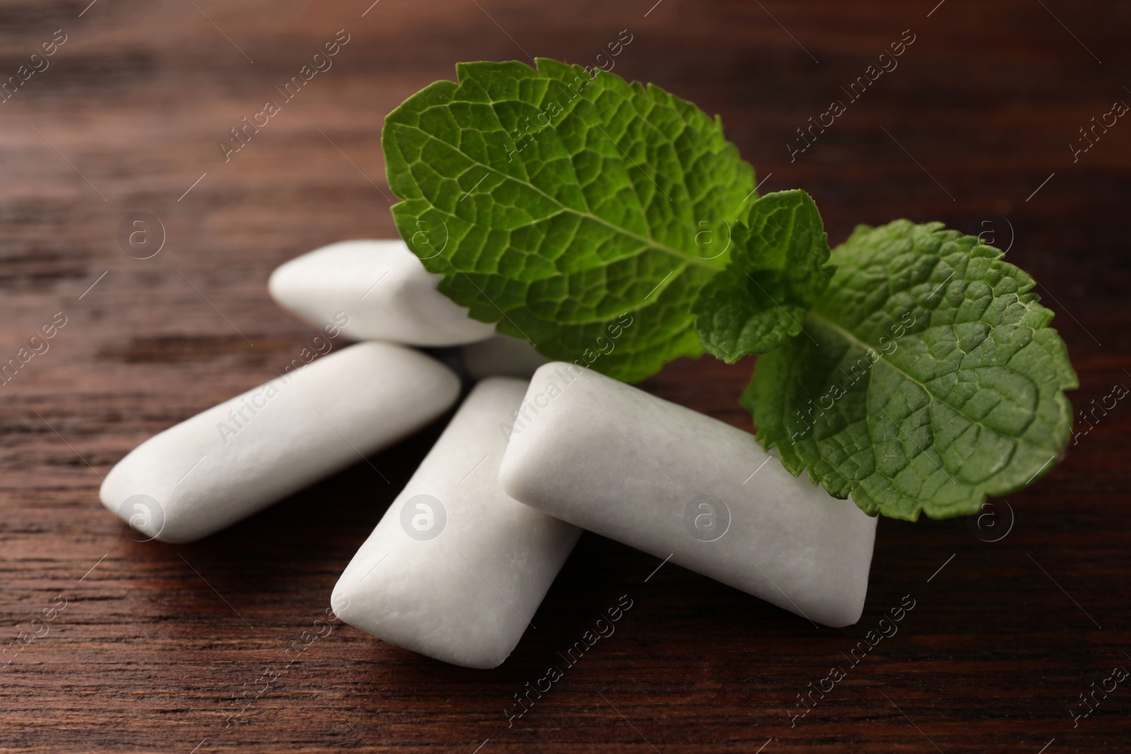 Photo of Tasty white chewing gums and mint leaves on wooden table, closeup