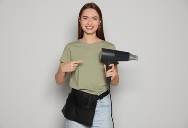 Photo of Portrait of happy hairdresser with hairdryer on light background