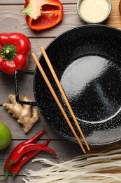 Black wok, chopsticks and products on color wooden table, flat lay