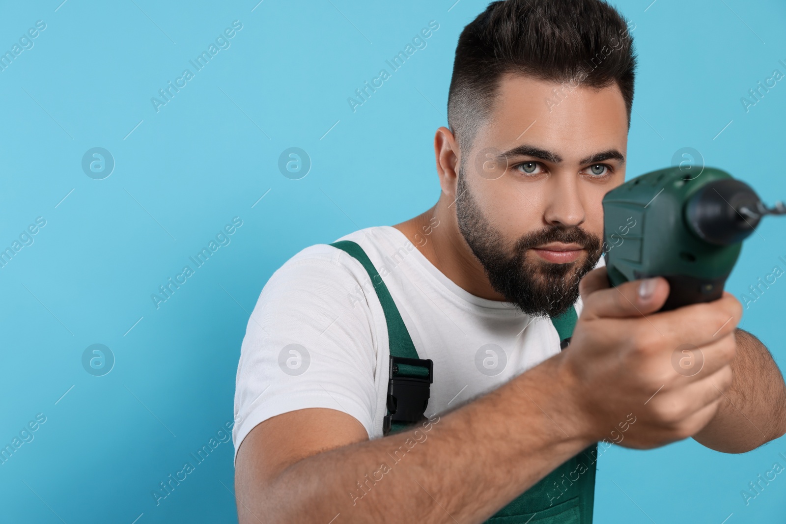 Photo of Young worker in uniform with power drill on light blue background. Space for text