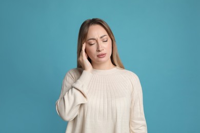 Young woman suffering from headache on light blue background