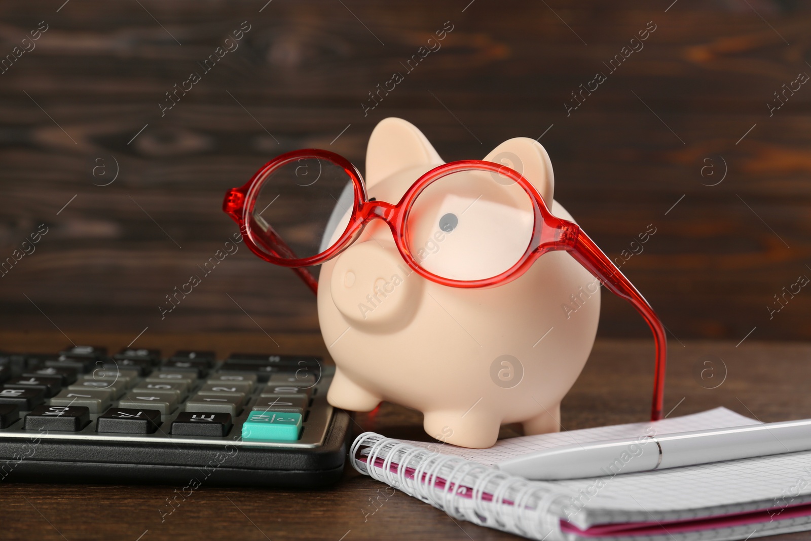 Photo of Calculator, notebook, pen and piggy bank with glasses on wooden table