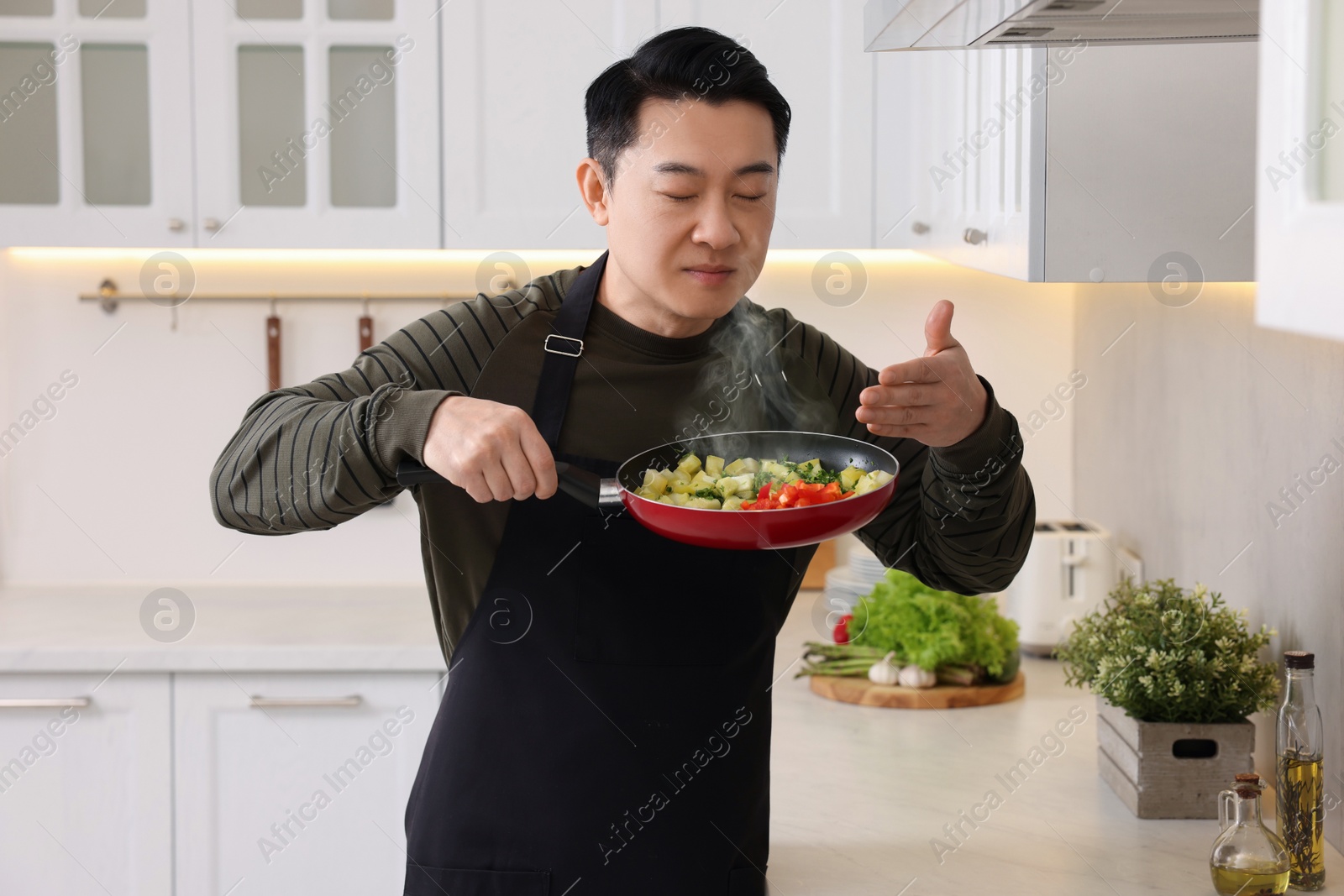 Photo of Man with frying pan smelling dish after cooking in kitchen