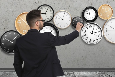 Image of Time management concept. Businessman and different clocks on light grey background