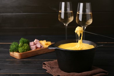 Photo of Dipping piece of ham into fondue pot with melted cheese on black wooden table