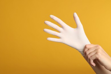 Doctor wearing medical gloves on yellow background, closeup. Space for text