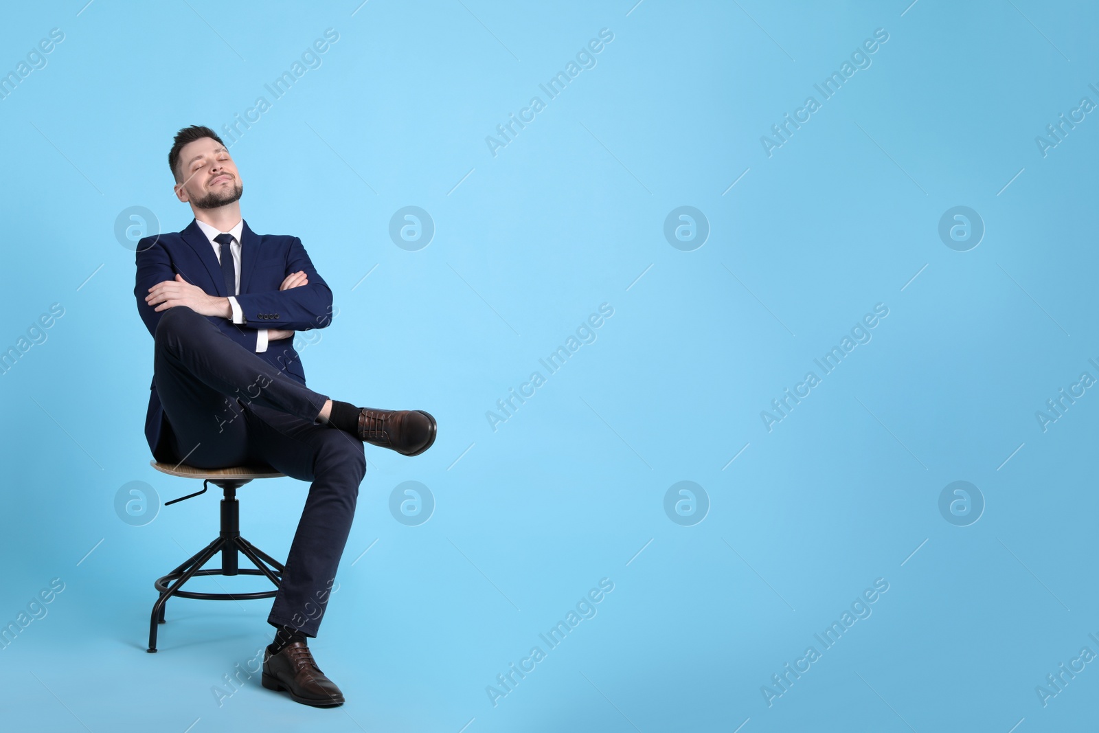 Photo of Handsome businessman relaxing in office chair on light blue background