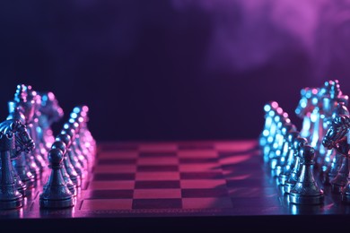 Set of chess pieces on checkerboard in color light before game, selective focus. Space for text