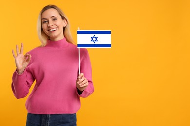 Happy young woman with flag of Israel showing OK gesture on yellow background