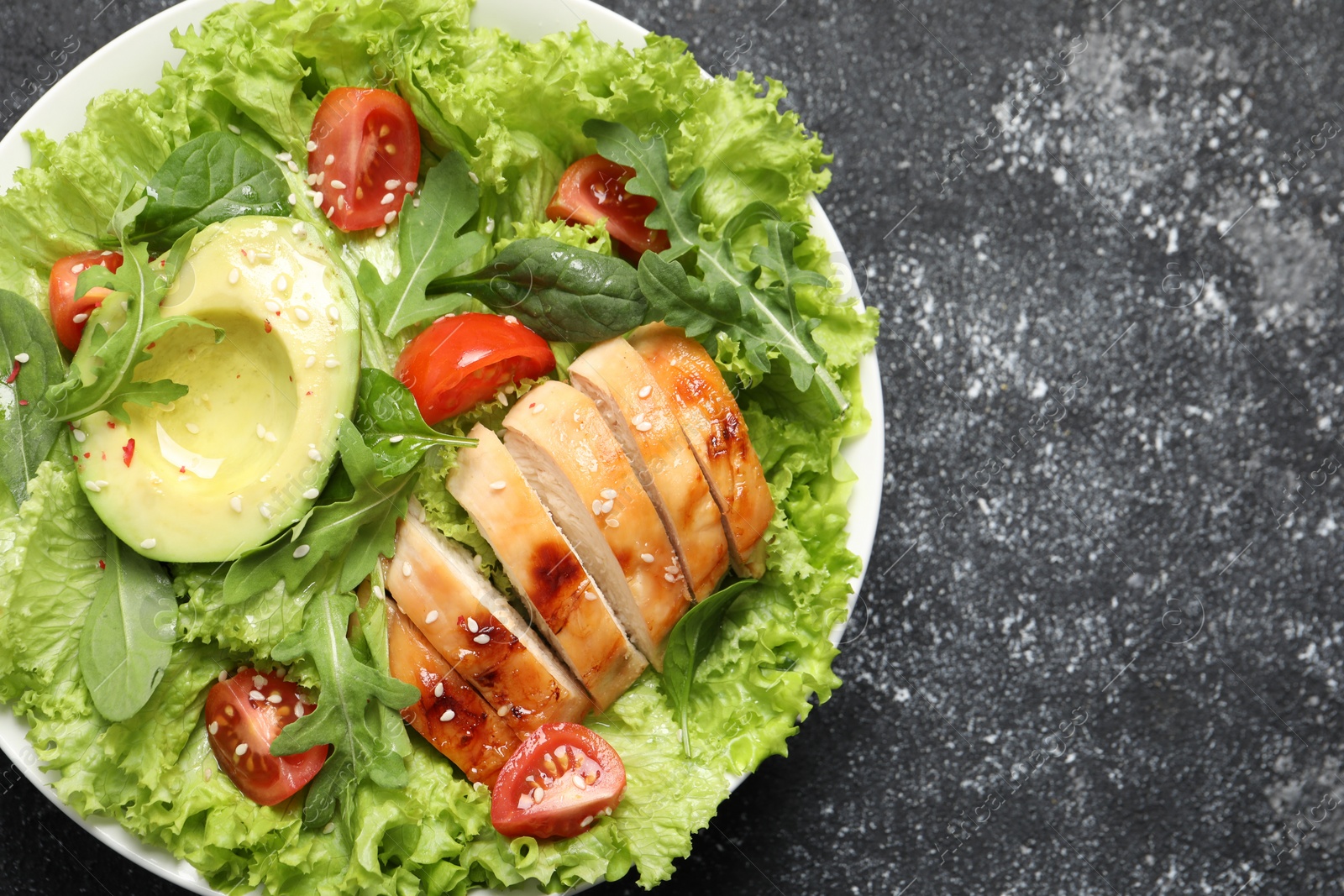 Photo of Delicious salad with chicken, cherry tomato and avocado on grey textured table, top view. Space for text