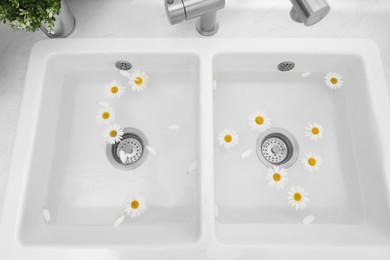Photo of Sink with water and beautiful chamomiles indoors, above view