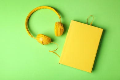 Photo of Modern headphones with hardcover book on color background, top view. Space for text