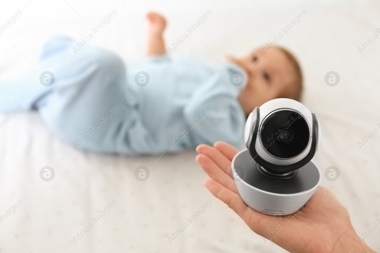 Photo of Woman holding baby camera near child on bed. Video nanny