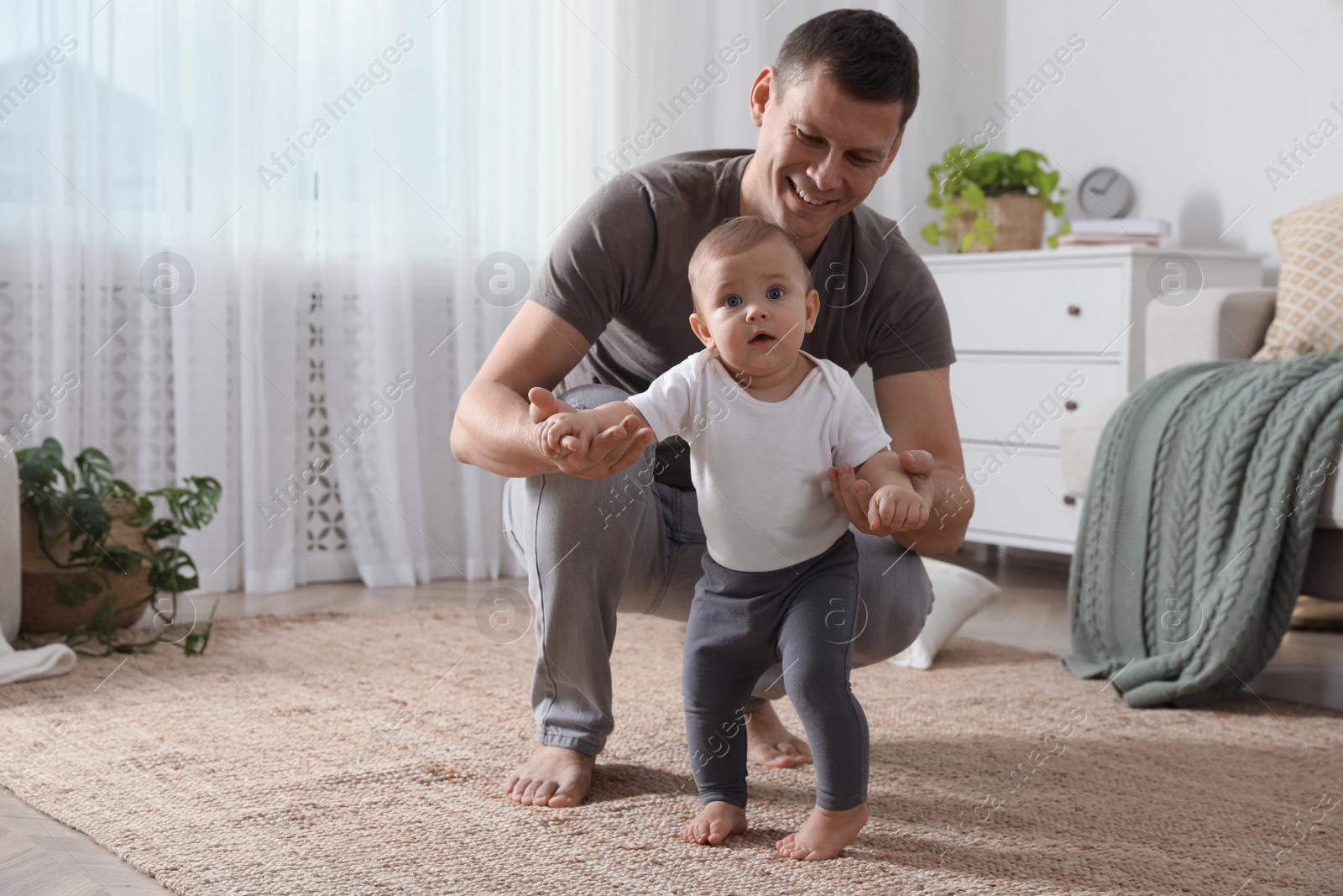 Photo of Father supporting his baby daughter while she learning to walk at home