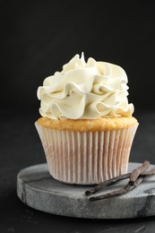 Photo of Tasty cupcake with cream and vanilla pods on black table, closeup