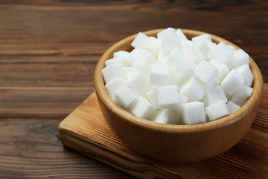 Photo of White sugar cubes in bowl on wooden table, closeup. Space for text