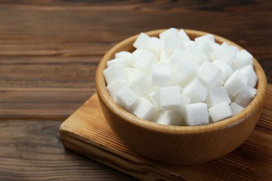 White sugar cubes in bowl on wooden table, closeup. Space for text