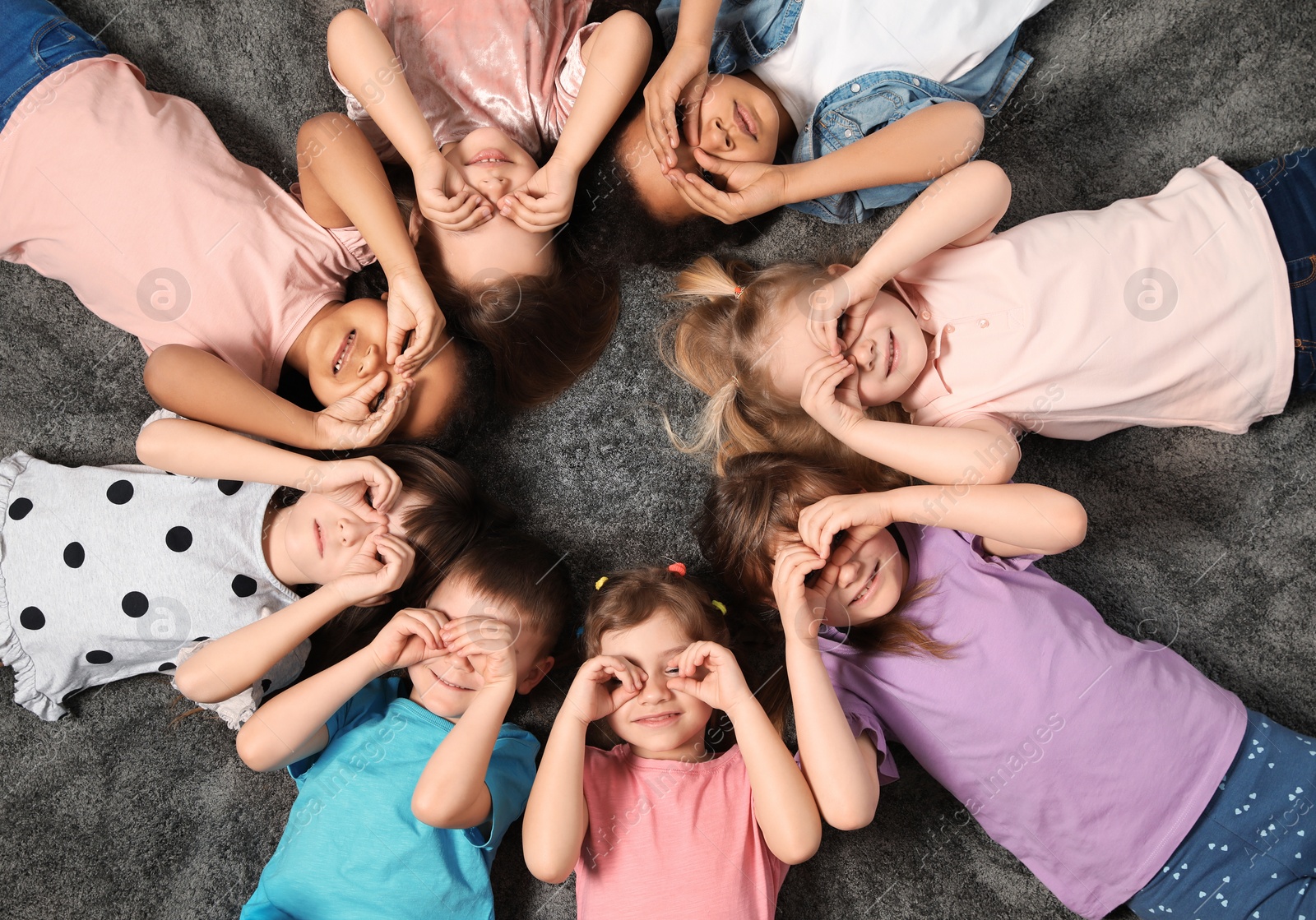 Photo of Little children lying on carpet together indoors, top view. Kindergarten playtime activities