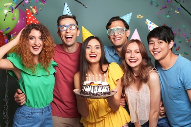 Young people celebrating birthday with tasty cake on color background