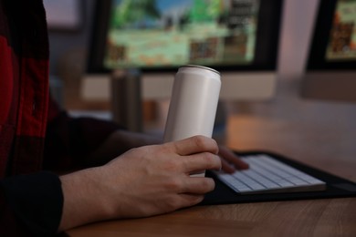 Photo of Young man with energy drink playing video game at wooden desk indoors, closeup