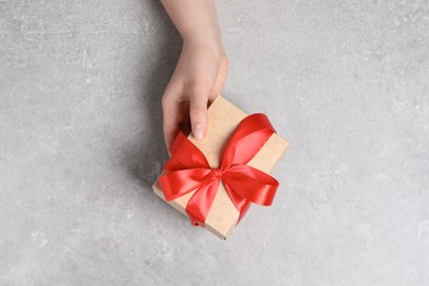 Woman holding gift box with red bow at light grey table, top view