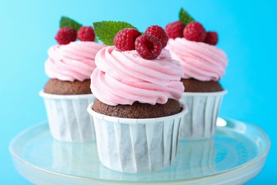 Photo of Delicious cupcakes with cream and raspberries on light blue background, closeup
