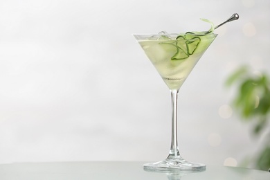 Photo of Glass of tasty cucumber martini on table against light background, space for text