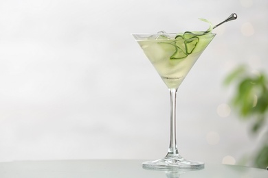 Glass of tasty cucumber martini on table against light background, space for text