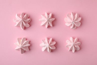 Many tasty meringue cookies on pink background, flat lay