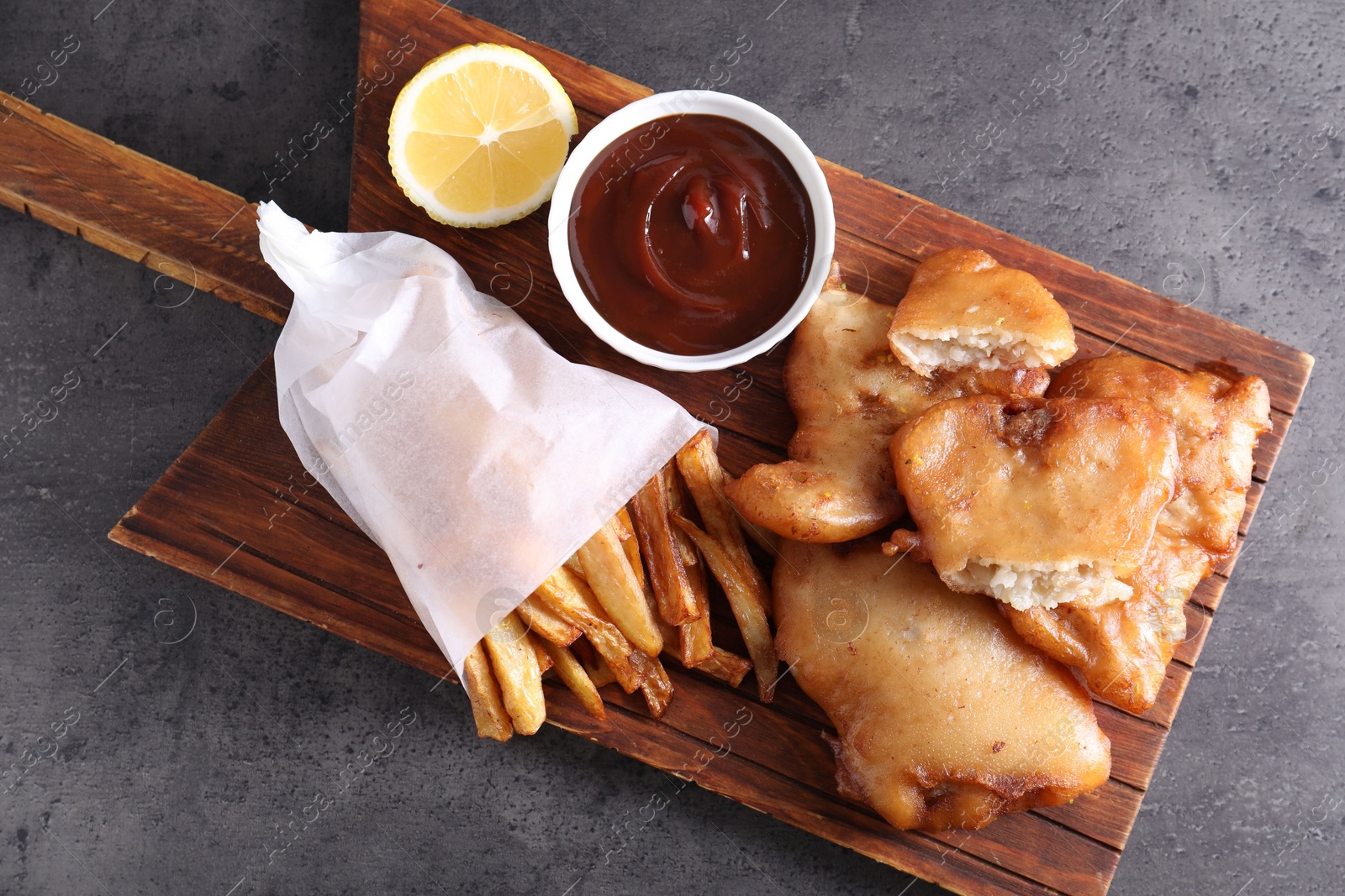 Photo of Tasty fish, chips and sauce on grey table, top view