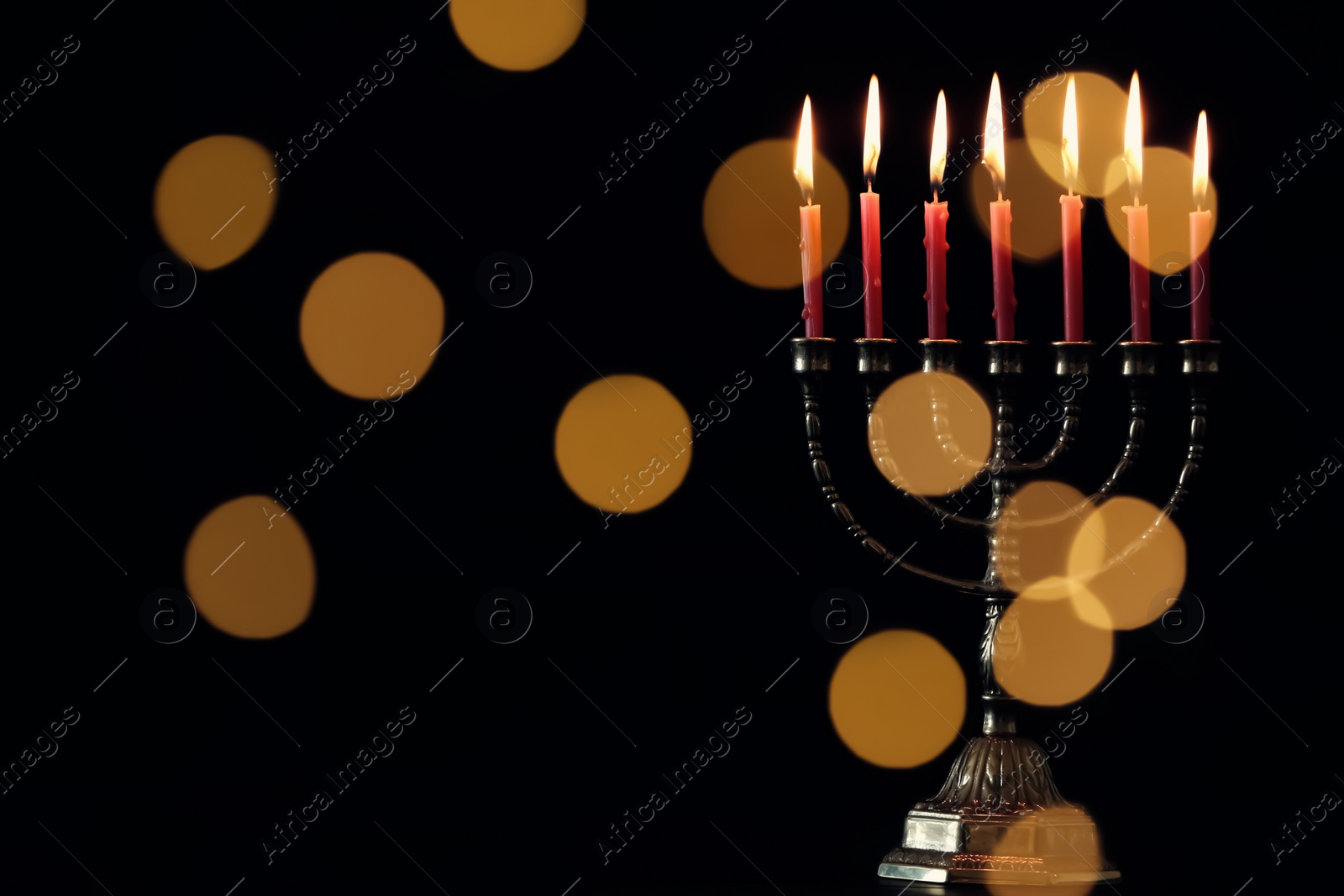 Photo of Golden menorah with burning candles against dark background and blurred festive lights, space for text